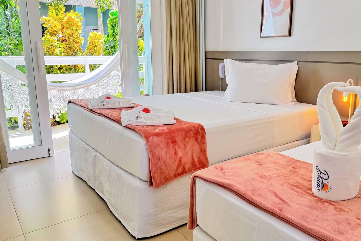 A hotel room with two beds, a balcony with plants, and a towel rack with towels.