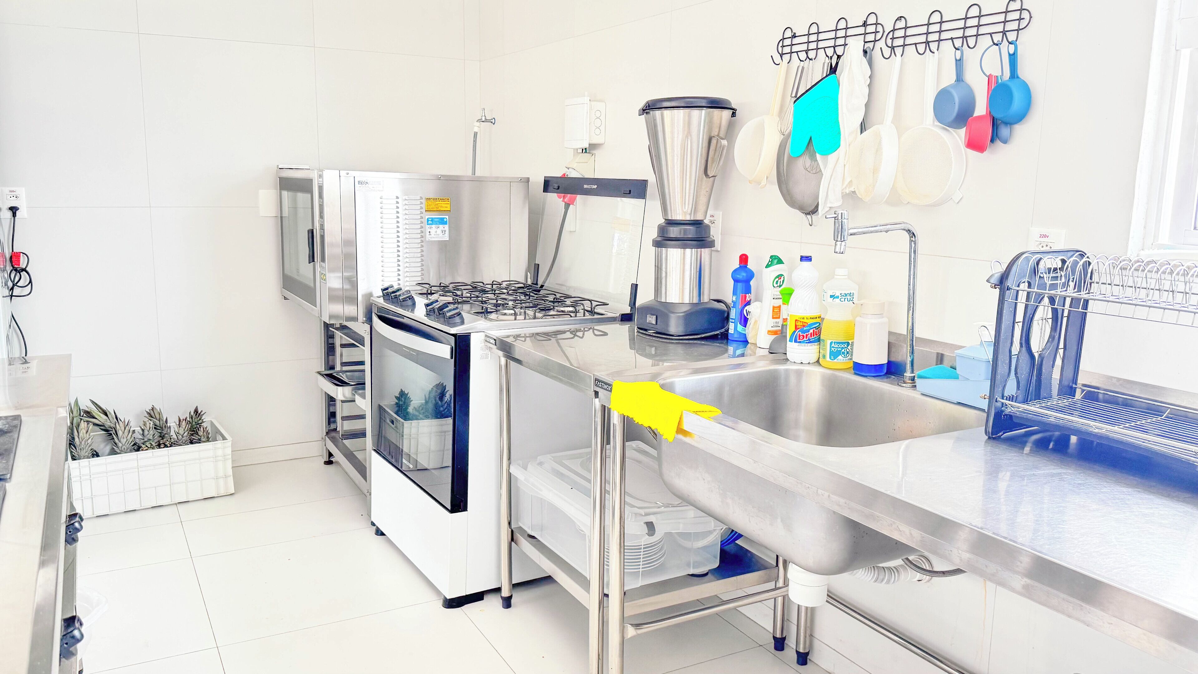 A commercial kitchen with stainless steel appliances, including a stove, oven, and sink, with various kitchen utensils and cleaning supplies.