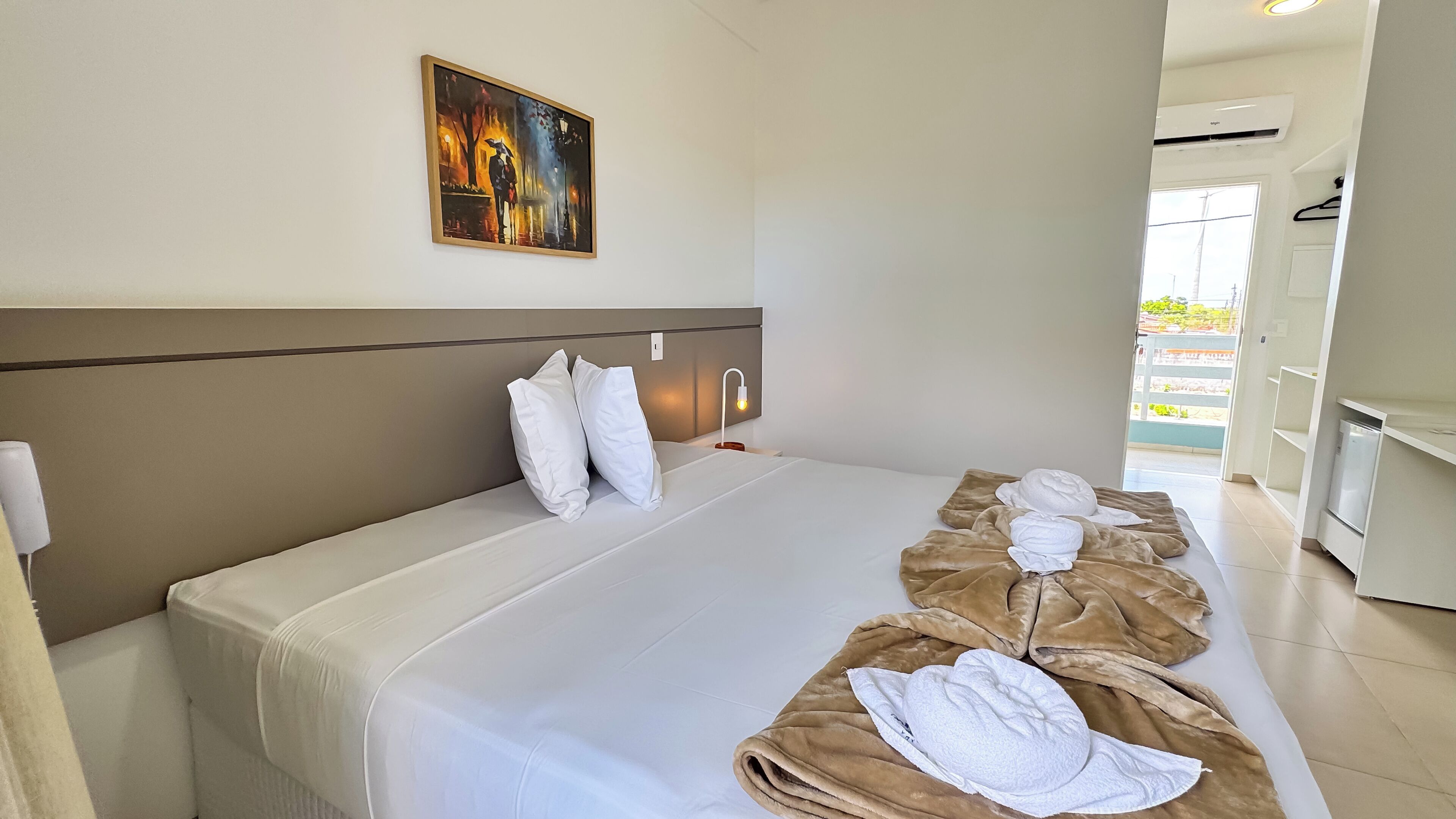 A hotel room with a large bed, a painting on the wall, and a view of the outside balcony.