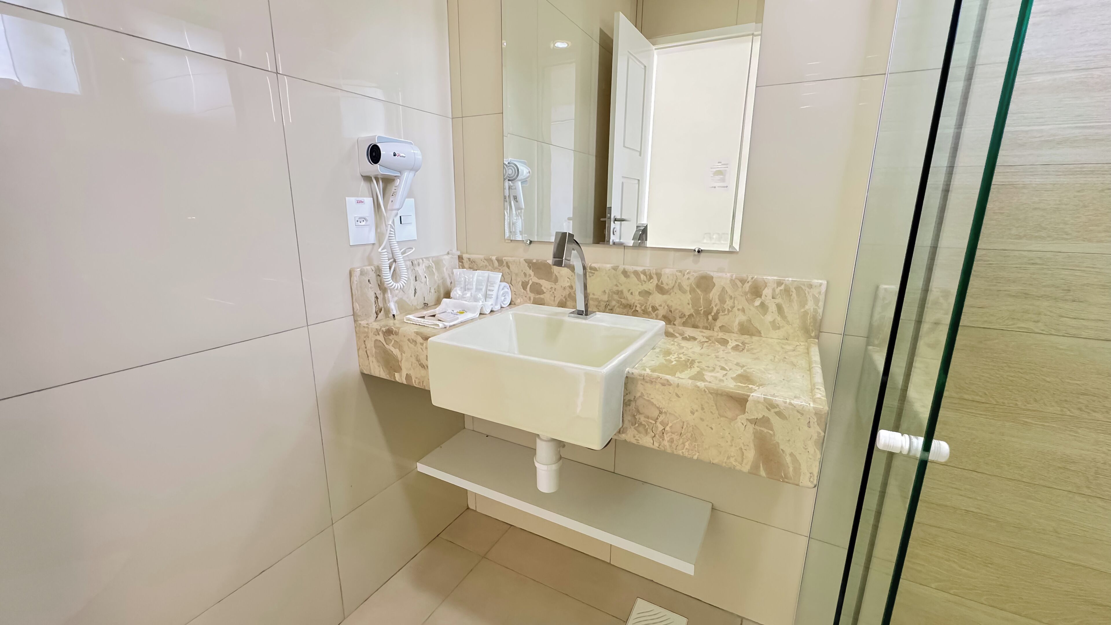 A modern bathroom with a white sink, a mirror, and a hairdryer mounted on the wall.