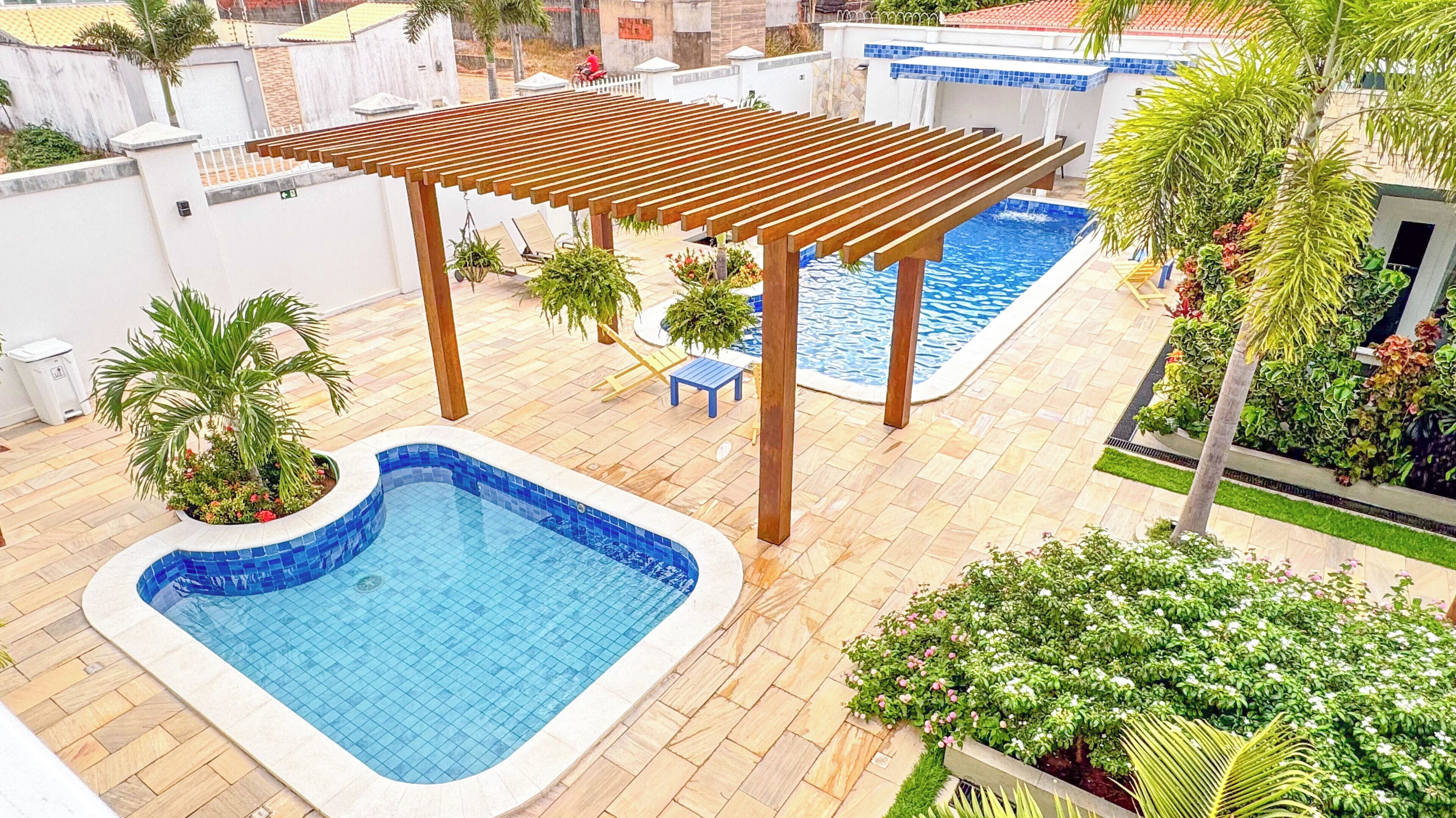 A rooftop pool area with two pools, a pergola, and surrounding greenery.