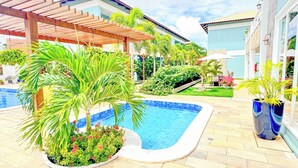 A swimming pool surrounded by lush greenery and a wooden pergola. - Pousada Diane (Trairi)