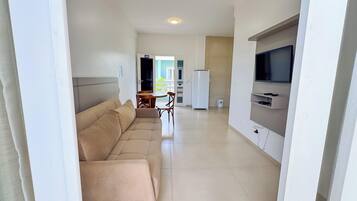 Un salon moderne avec un canapé beige, un coin repas comprenant une table et des chaises, un réfrigérateur et un téléviseur fixé au mur.