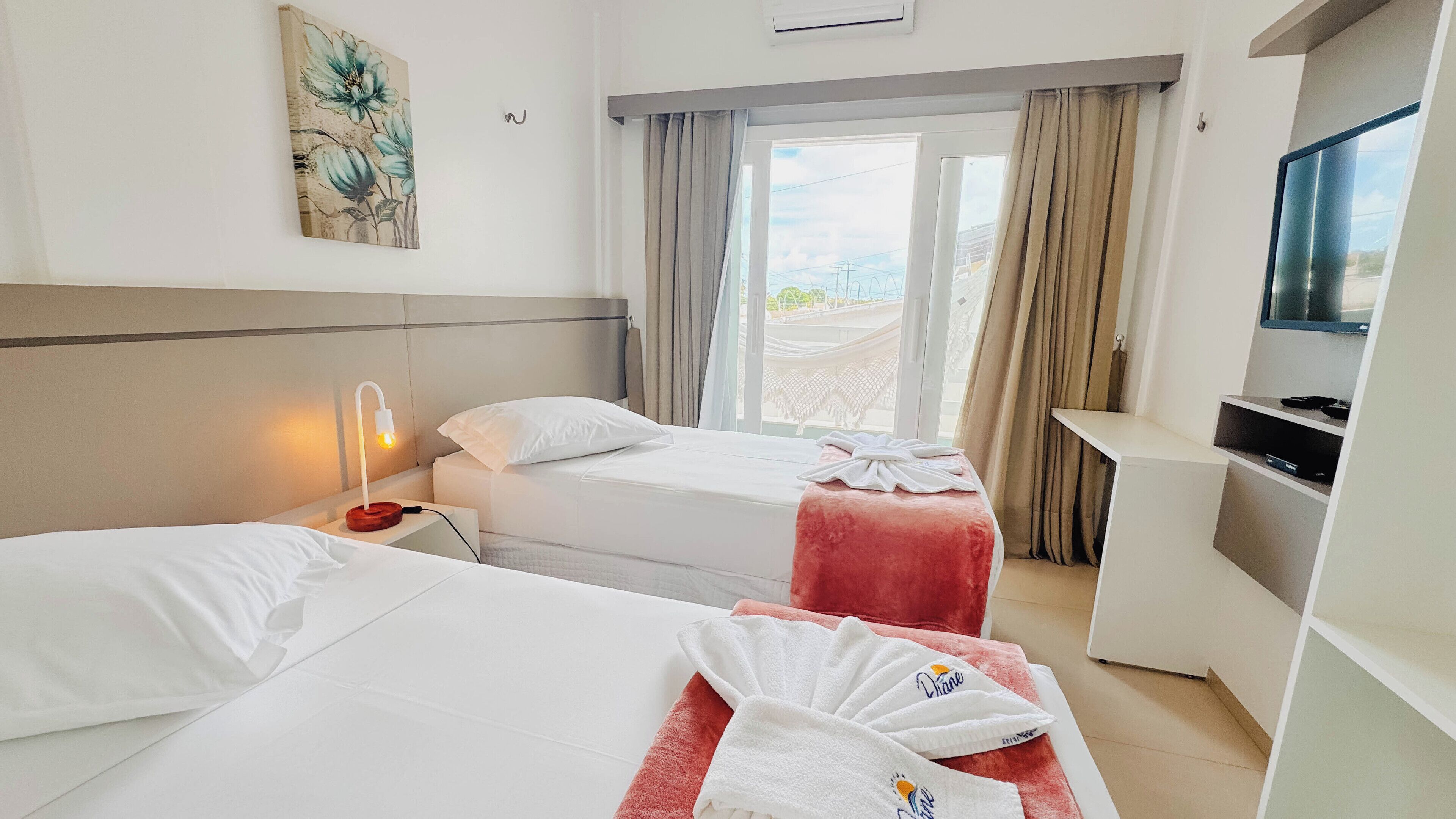 Una habitación de hotel con dos camas, un escritorio, un televisor y una ventana con cortinas.