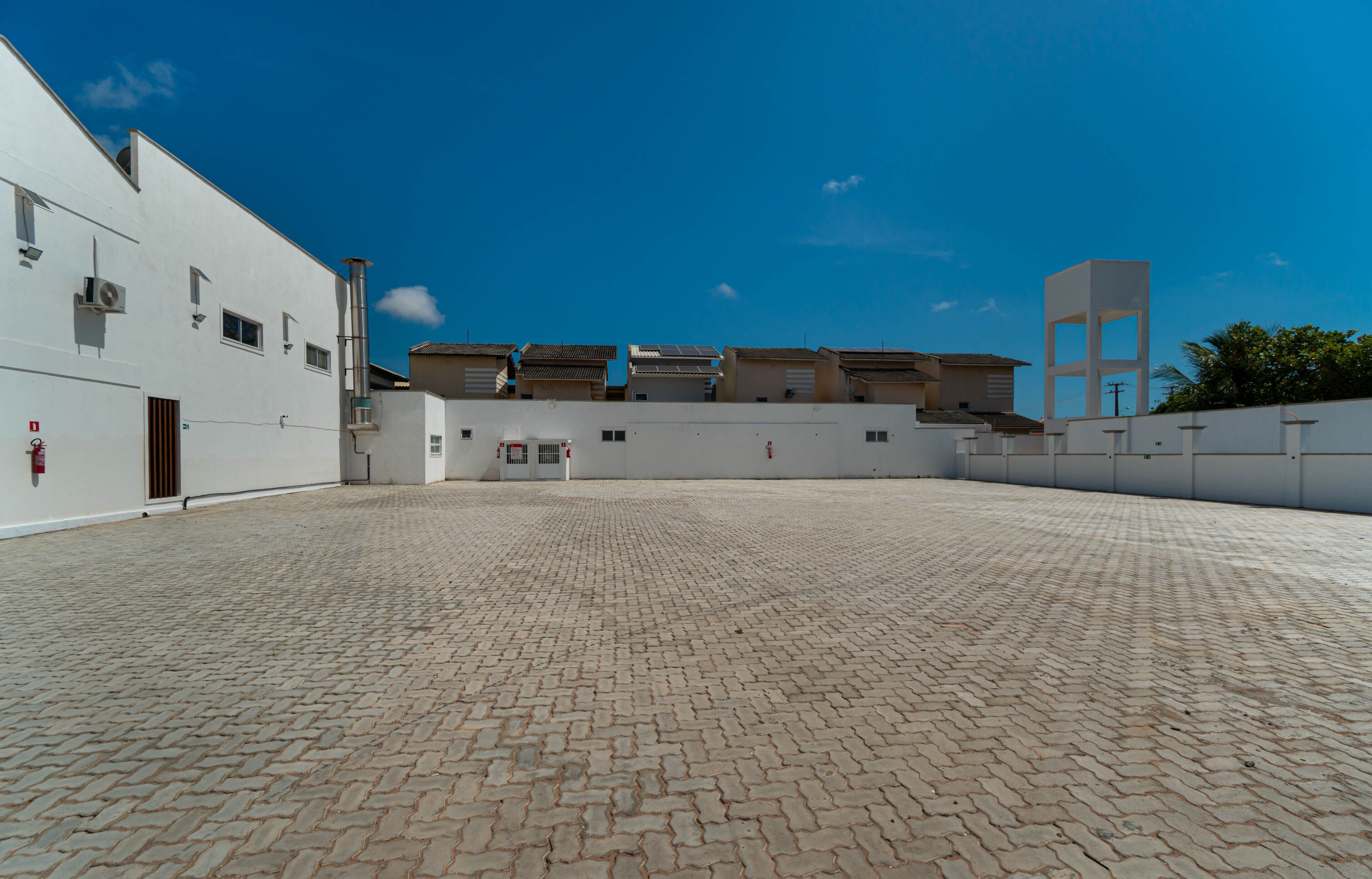 A spacious courtyard with a paved floor, white buildings, and a clear blue sky.
