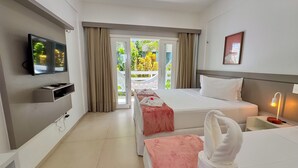 A hotel room with a bed, a TV, a bedside table with a lamp, a window with curtains, and a view of greenery outside. - Pousada Diane (Trairi)