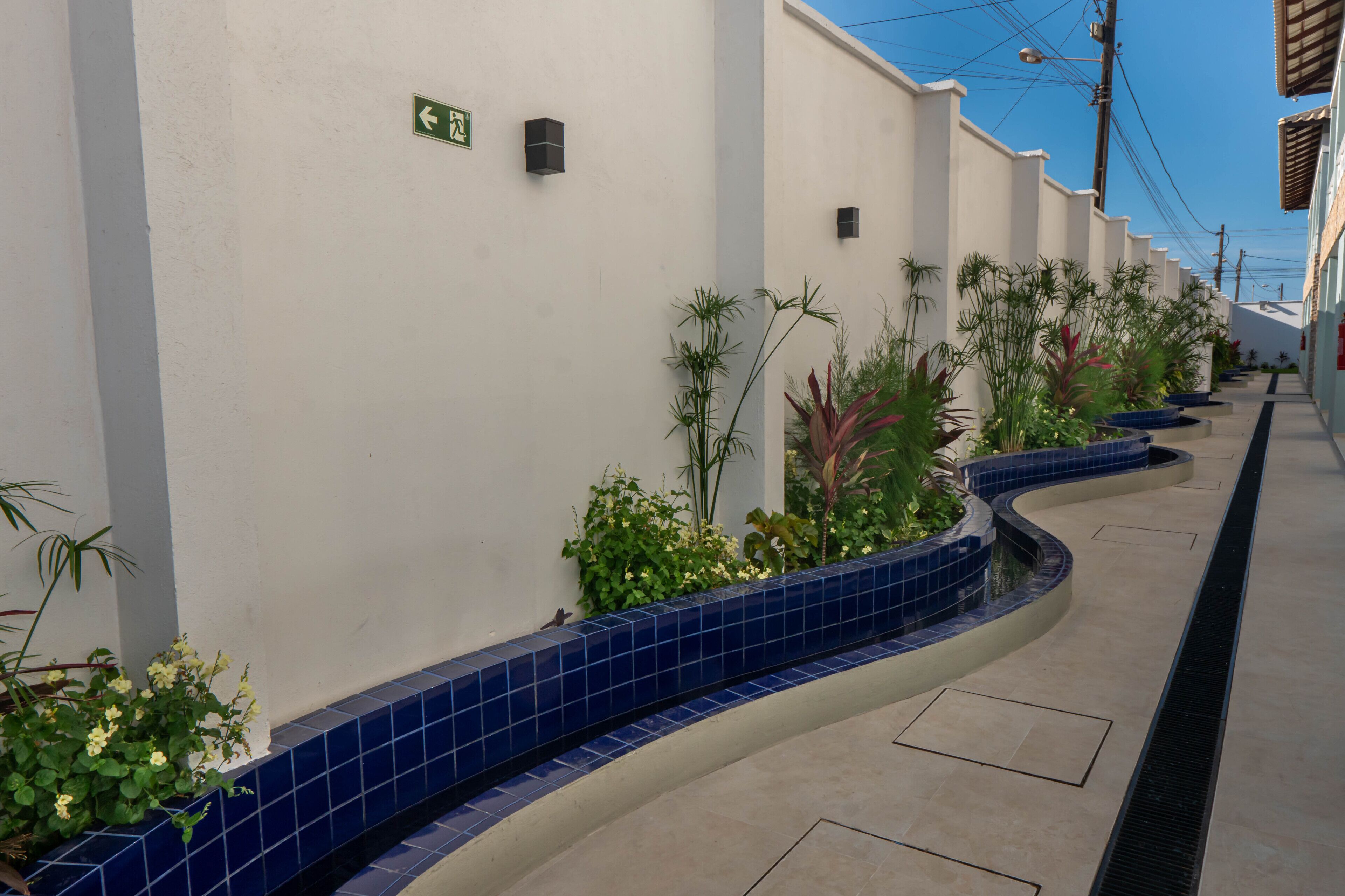 Un pasillo con una jardinera azul de azulejos con plantas, una pared blanca y un letrero direccional verde.