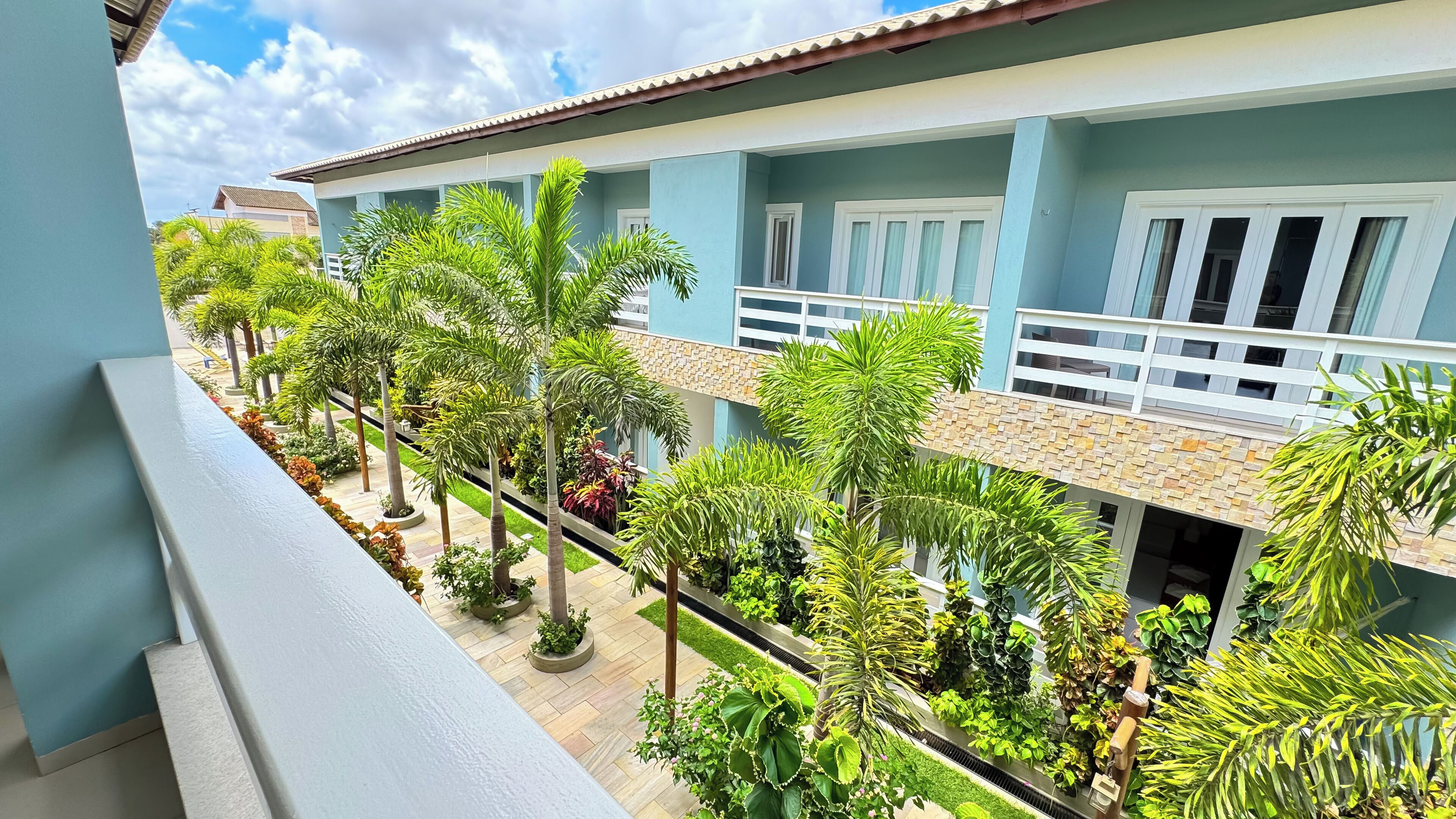 A residential building with a balcony overlooking a well-maintained garden with various plants and a tiled roof.