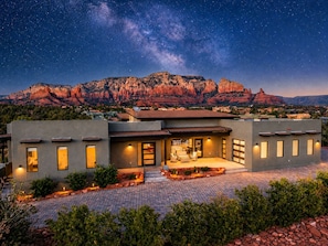 A modern house with a patio, a mountain backdrop, and a starry sky.