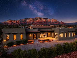 Ein modernes Gebäude mit einer Terrasse, einer Satellitenschüssel und Blick auf rote Felsformationen unter einem sternenübersäten Himmel.