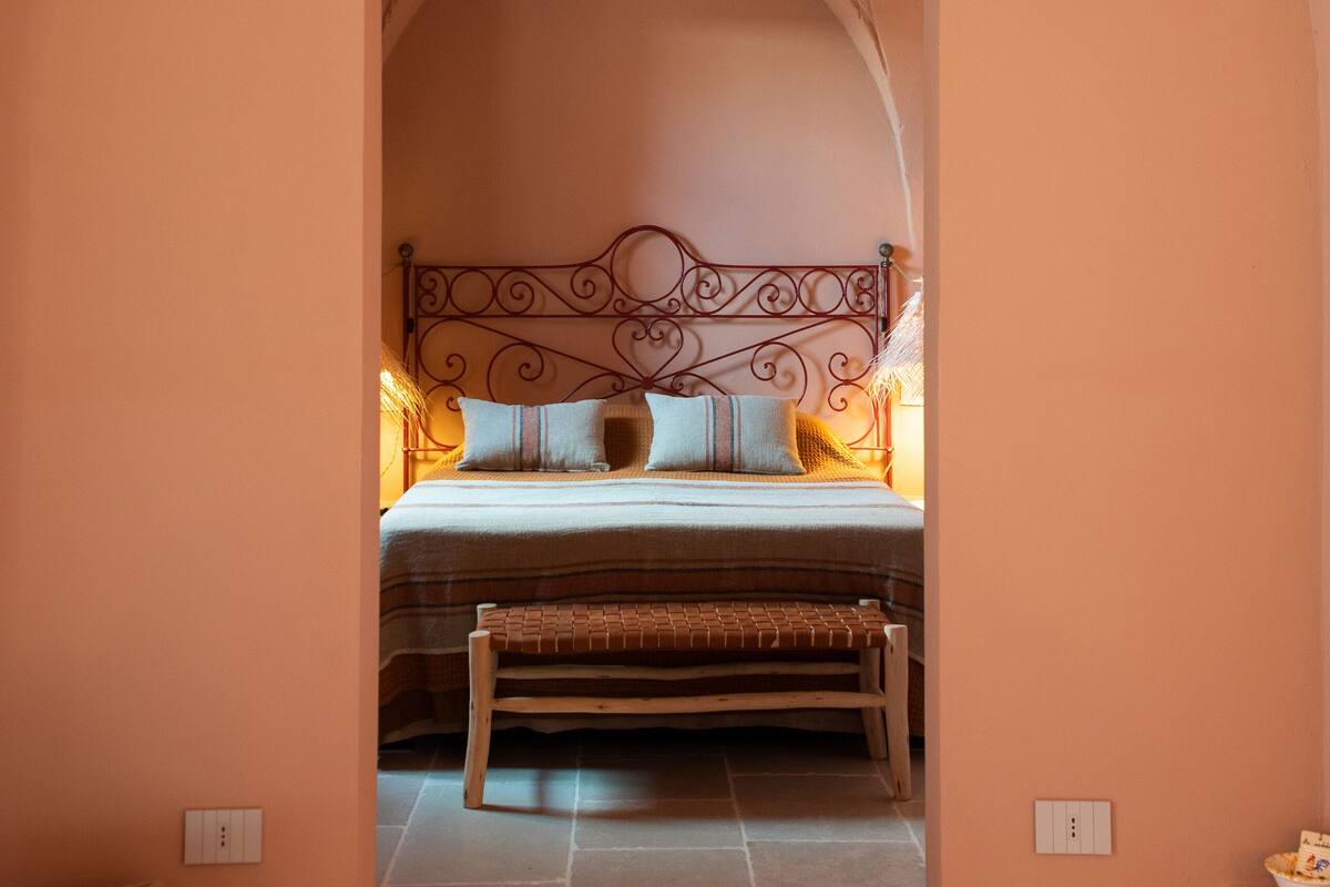 Een slaapkamer met een bed, een bankje en een lamp.