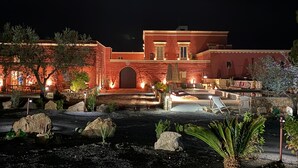 Een gebouw met een grote, gewelfde ingang, terras en een zwembad bij nacht.