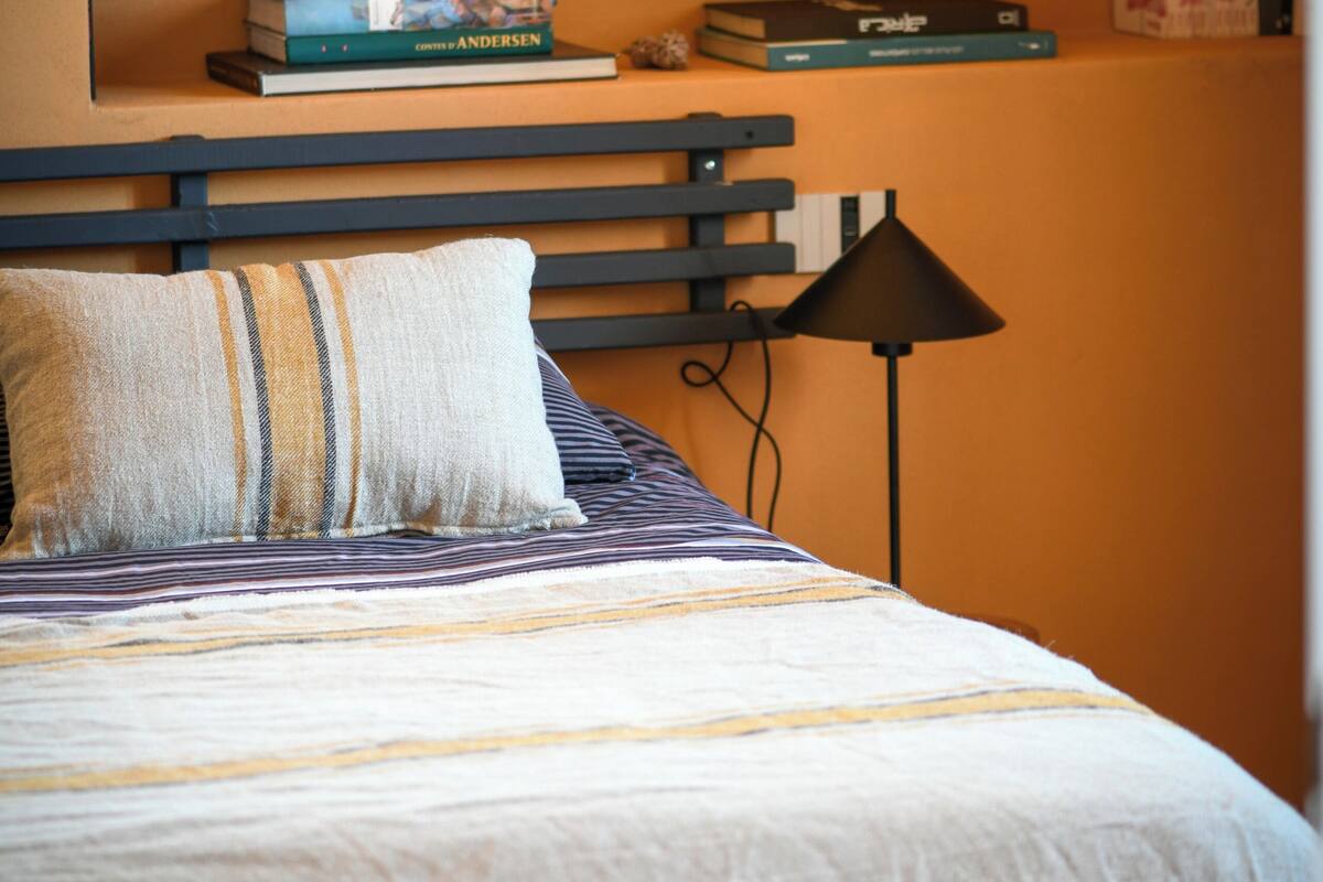 Een opgemaakt bed met streepjesbeddengoed, een kussen en een bedlampje.
