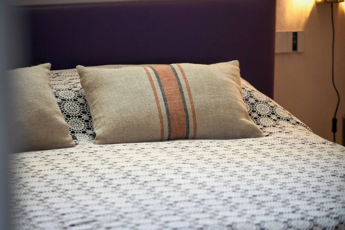 Een net opgemaakt bed met een gestreept beddegoed en meerdere kussens.