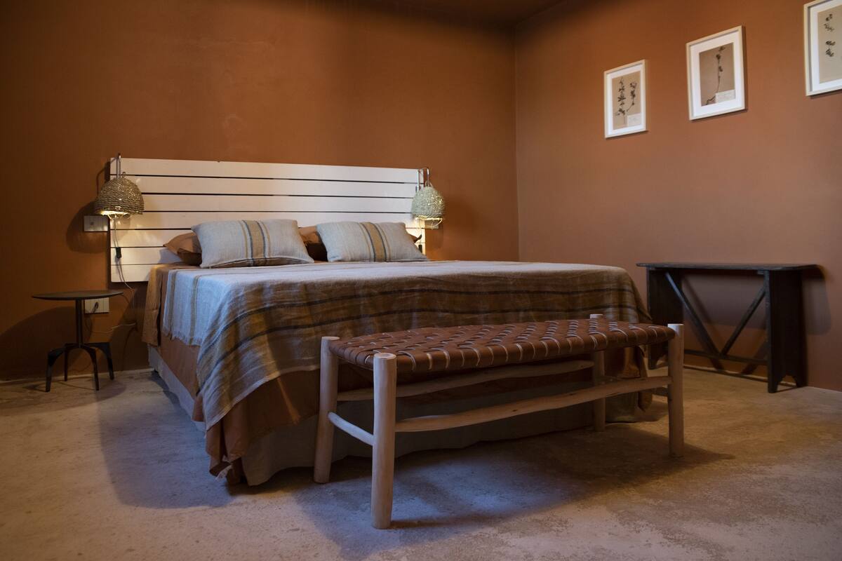 Een slaapkamer met een bed, nachtkastjes, een bankje en fotolijstjes aan de muur.