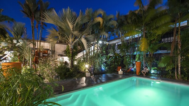 Una piscina rodeada de palmeras y follaje, con una escalera que conduce a un nivel superior.