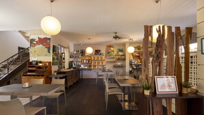Un restaurante moderno con zona de comedor central, barra y cocina. Destacan detalles de madera y lámparas colgantes.