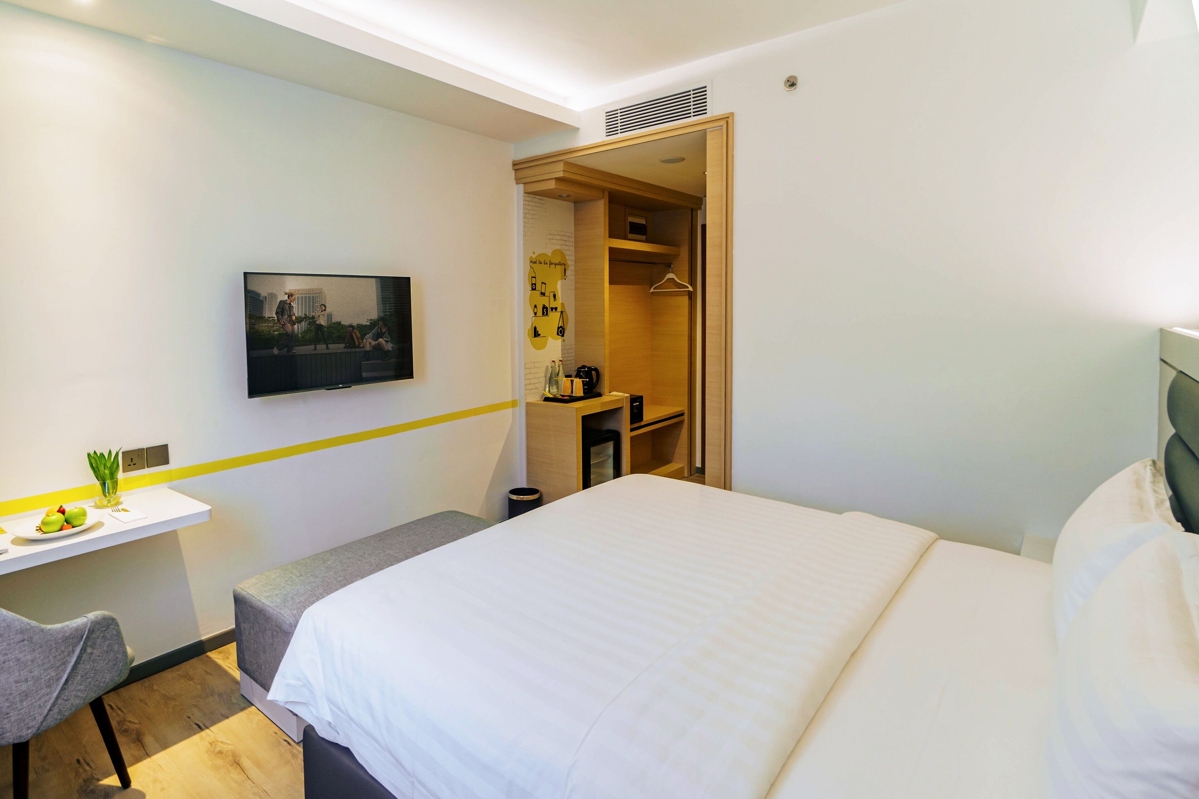 Habitación de hotel con cama, escritorio, silla, televisor montado en la pared y armario.