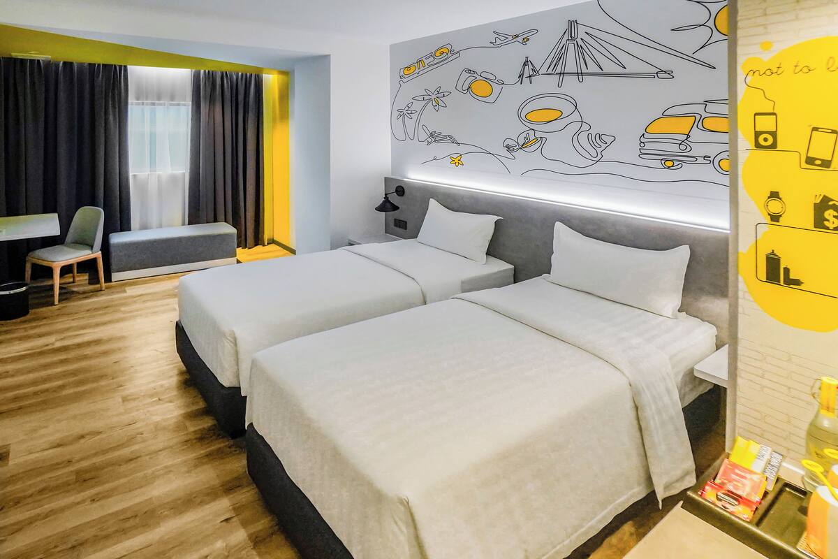 A hotel room with two beds, a desk, a chair, and a wall mural.