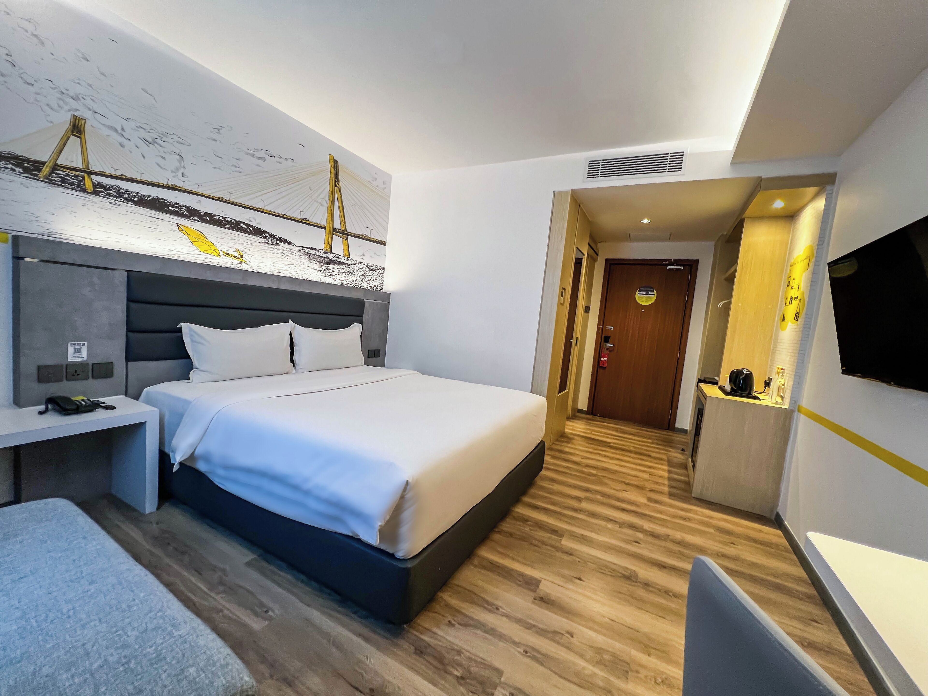 A modern hotel room with a large bed, a desk, a flat-screen TV, and a wooden floor.