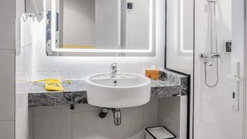 A modern bathroom with a large mirror, white sink, and a glass-enclosed shower.