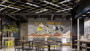 A modern restaurant interior with a central dining area, high ceiling with exposed beams, and a mural on the back wall. - YELLO Hotel Harbour Bay Batam (Batam)