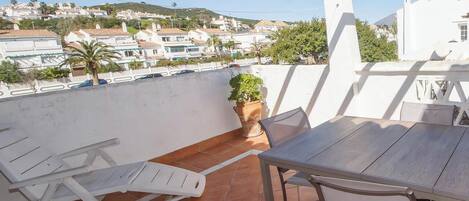A terrace with a table and chairs, a potted plant, and a view of a residential area.