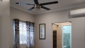 A bedroom with a bed, a ceiling fan, a window with curtains, a framed picture on the wall, and a staircase leading to another room. - 4 Bedrooms Family House Sakumono (Sakumono)
