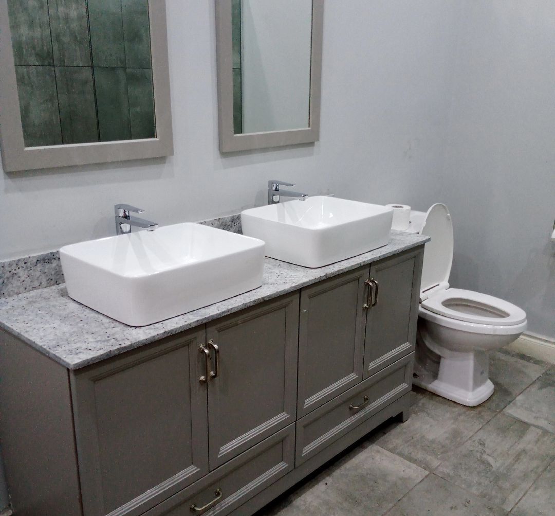 A bathroom with two white sinks, a toilet, and a cabinet with drawers.
