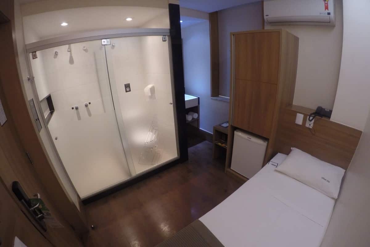 A hotel room with a bed, a wardrobe, a small desk, and a mirror.