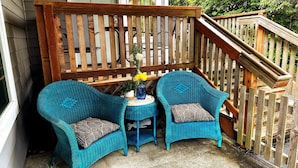 A wooden deck with two blue wicker chairs and a small table, a potted plant, and a wooden staircase. - Sea Glass Inn (Seaside)