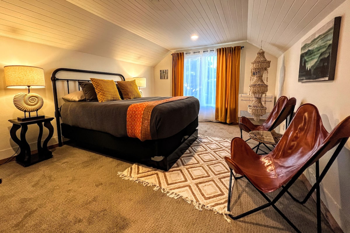 A bedroom with a bed, a nightstand, a lamp, a chair, and a window with curtains.