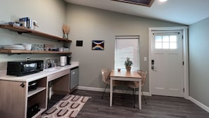 A compact kitchen with a microwave, coffee maker, and a dining area with a table and chairs. - Sea Glass Inn (Seaside)