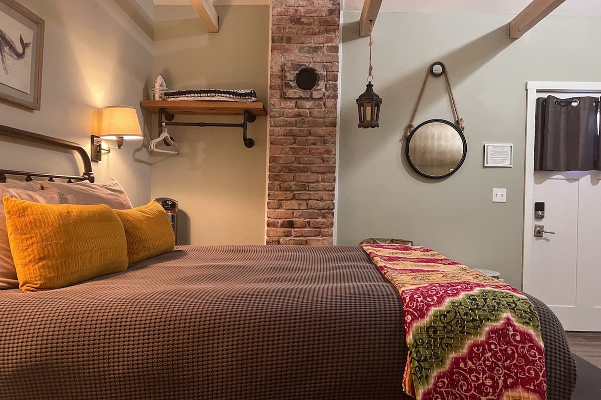 A bedroom with a bed, a nightstand, a lamp, a mirror, and a door.