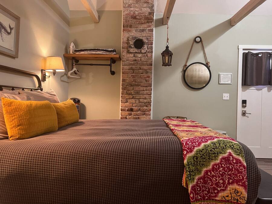 A bedroom with a bed, a nightstand, a lamp, a mirror, and a door.