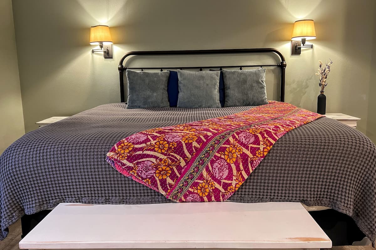 A neatly made bed with a patterned bedspread, two pillows, and a bedside table with a lamp.