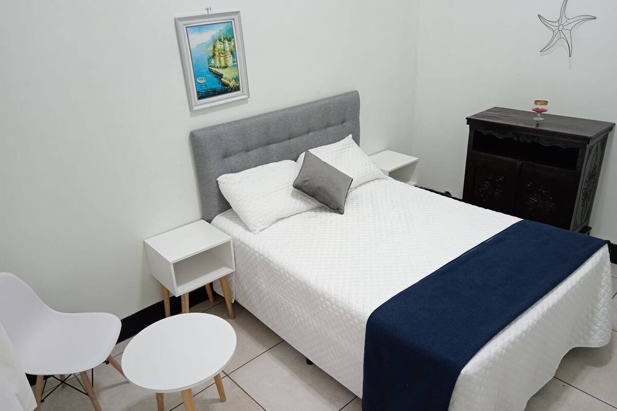 Une chambre bien rangée, avec un lit, deux tables de chevet, une chaise et une petite table.
