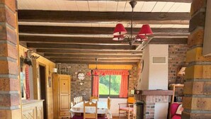 A rustic interior with exposed wooden beams, a dining area with a table and chairs, a fireplace, and a cozy seating area.