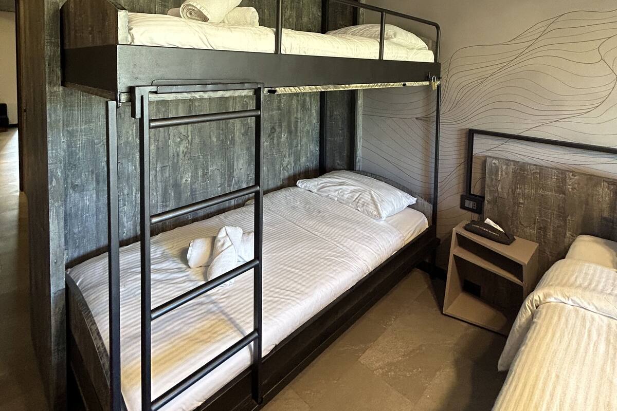 A bunk bed room with a wooden headboard, a bedside table with a lamp, and a wall art piece.
