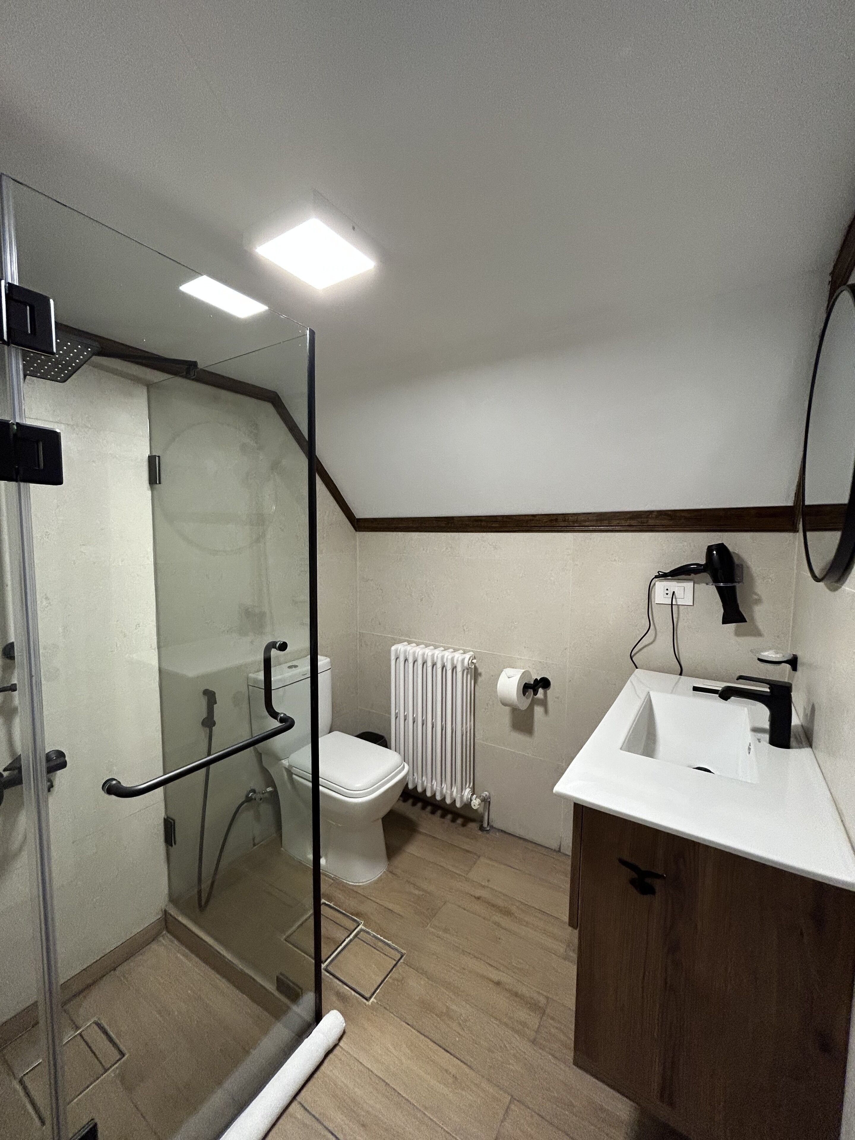 Een moderne badkamer met een douchecabine van glas, een wit toilet, een witte wastafel en een houten opbergmeubel.