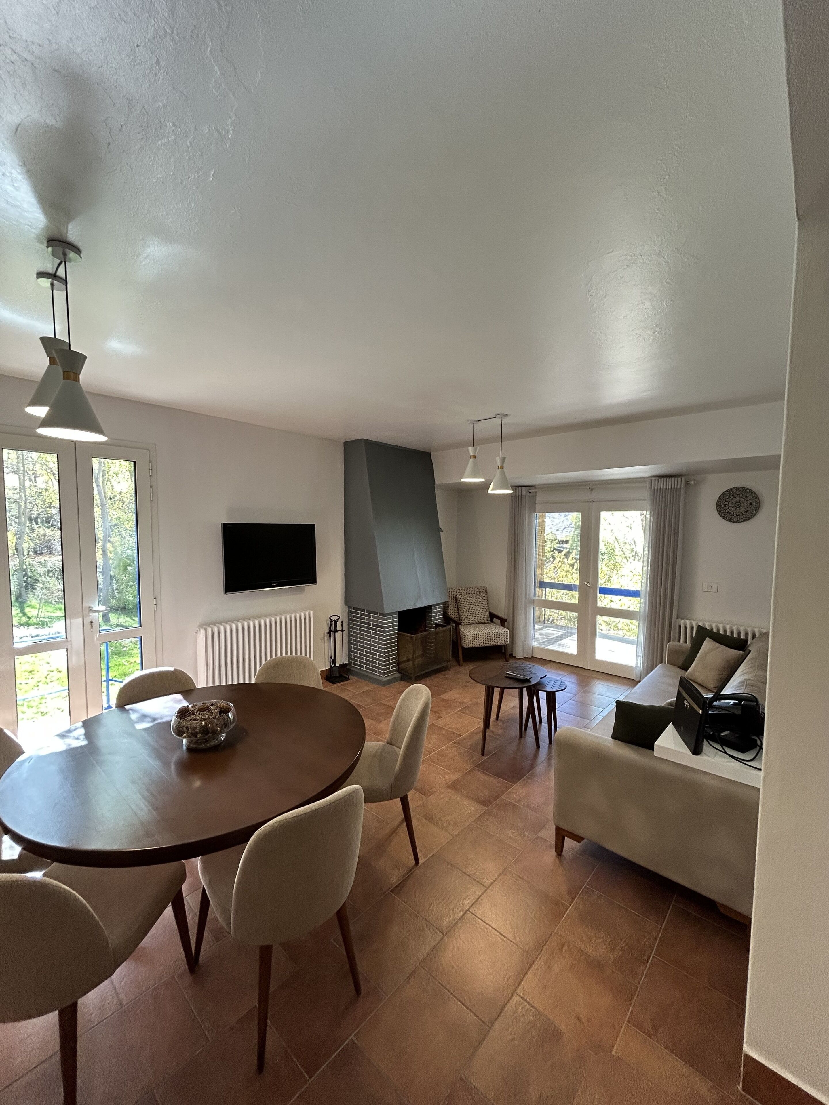 A spacious living area with a fireplace, a dining table with chairs, a sofa, and a TV mounted on the wall.