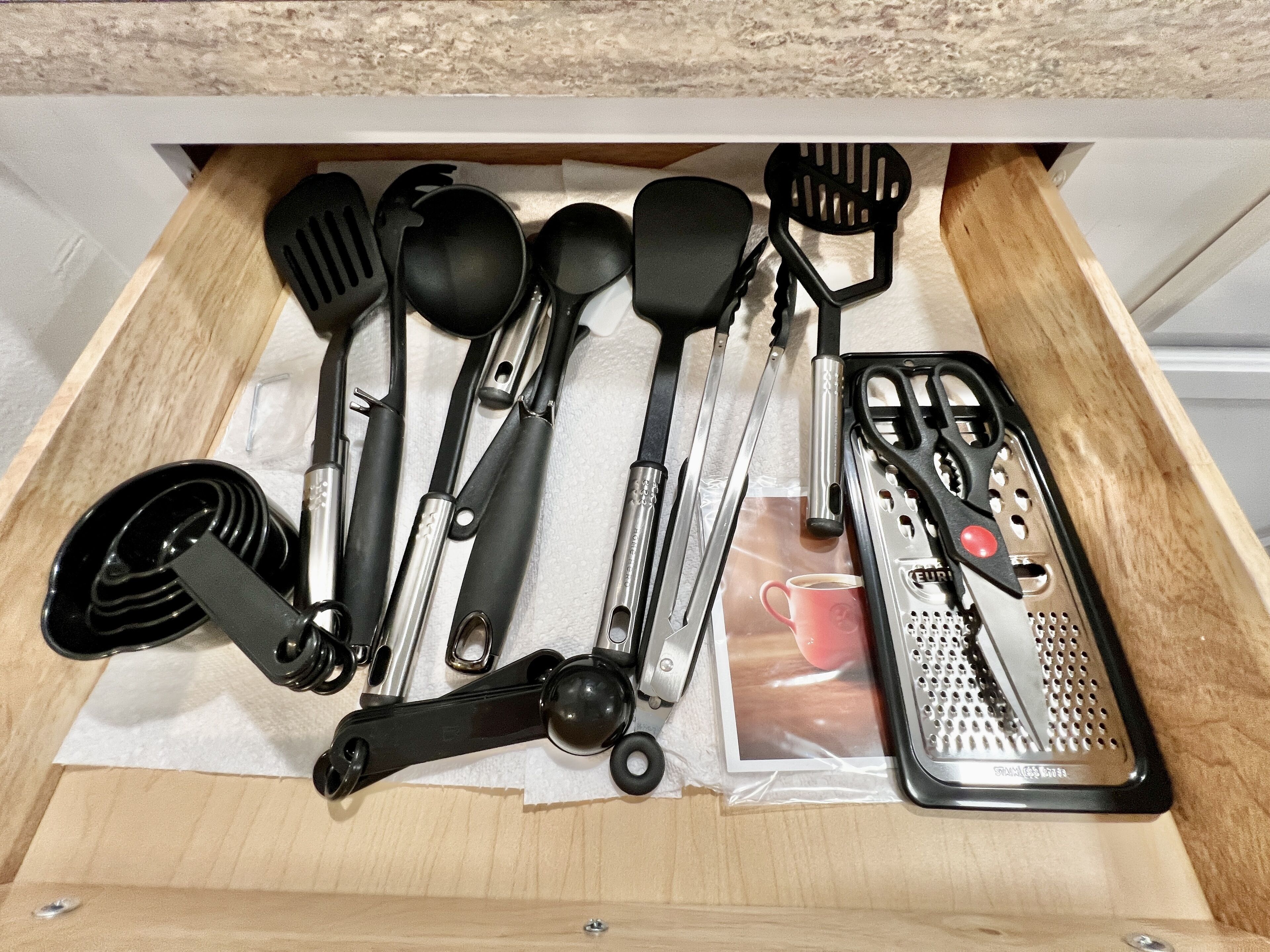 A drawer containing various kitchen utensils including spatulas, tongs, and a grater.