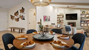 Ein modernes Wohnzimmer mit einem runden Esstisch, gemütlicher Sitzecke, Kamin und Fernseher.