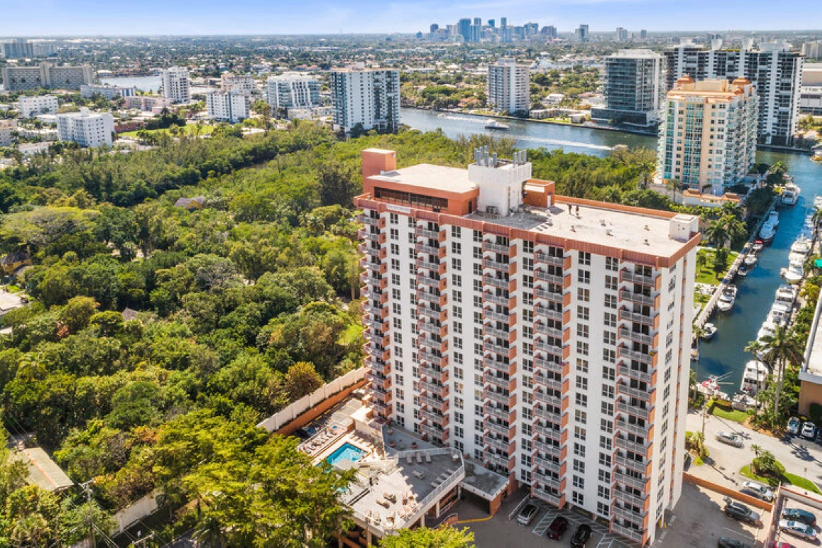 A high-rise building with multiple floors, surrounded by lush greenery and a river.