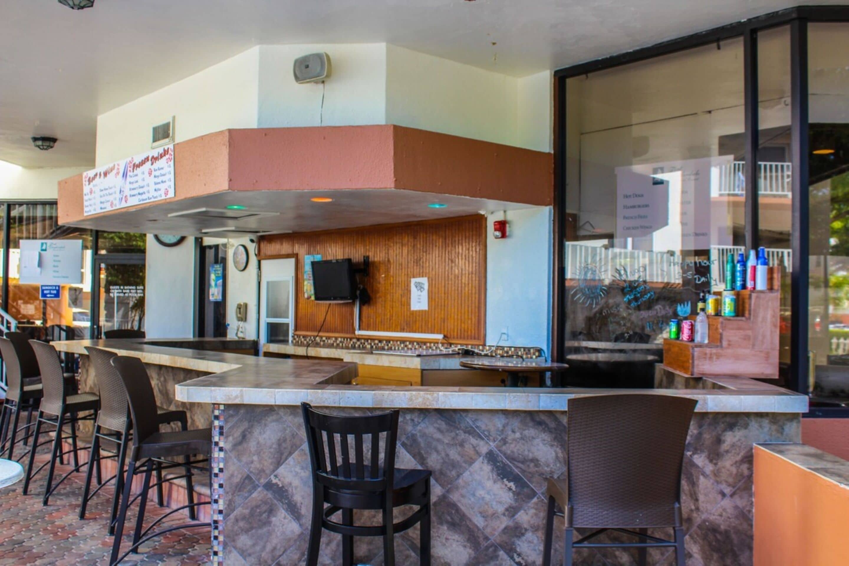 A restaurant with a counter, chairs, and a menu board.