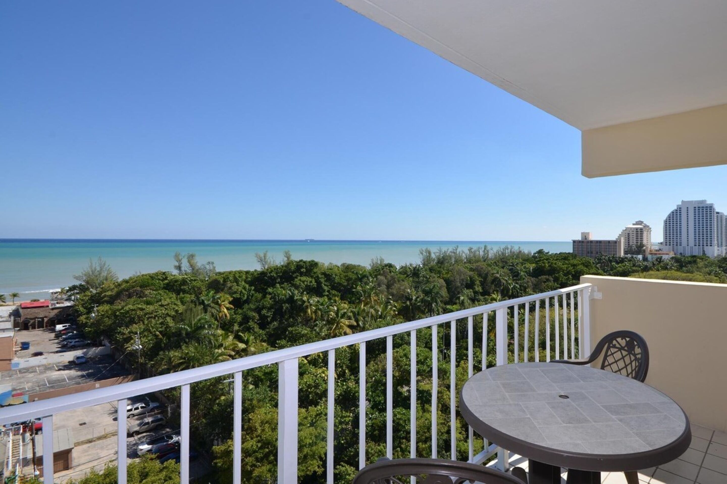 A balcony with a table and chairs overlooking a beach and cityscape.
