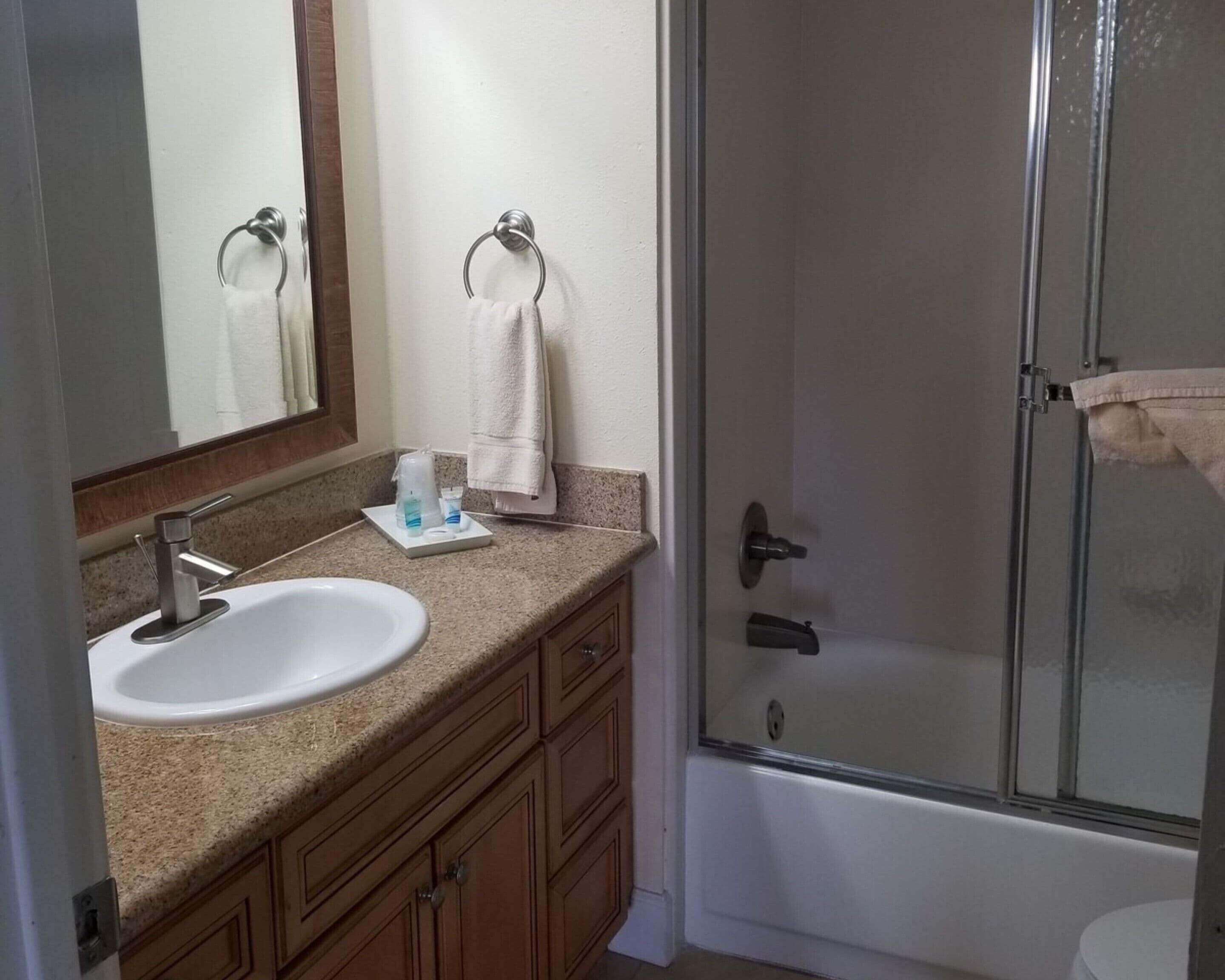 Un baño con lavamanos, espejo, toallero y ducha.