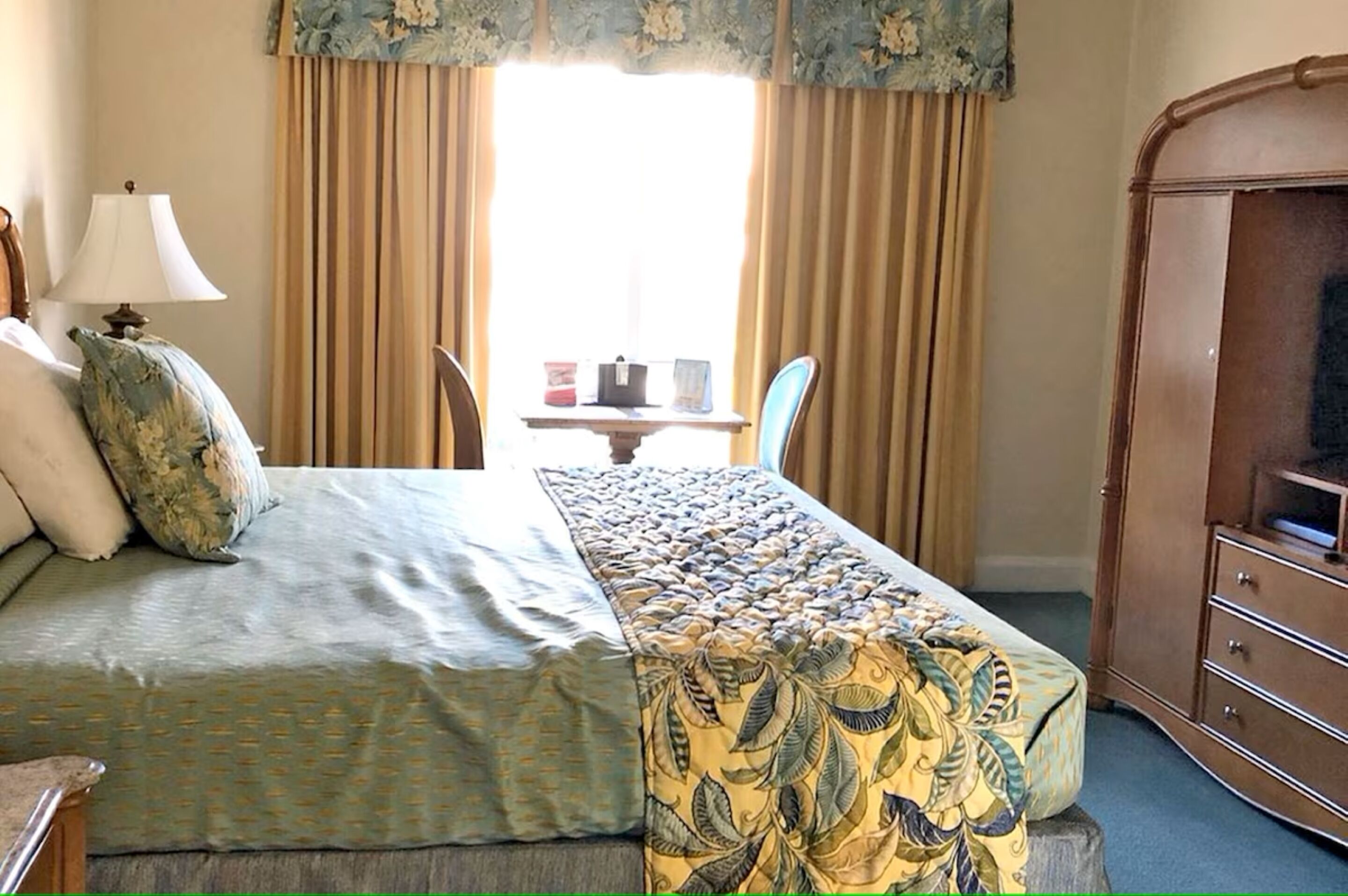 A hotel room with a bed, a table with a lamp, and a wardrobe.