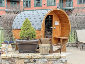 Eine Sauna mit Holzfassade, einem großen Topfpflanzen, Steinsitzen und einem Schild mit Sicherheitsanweisungen.