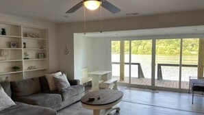 Ein Wohnzimmer mit Deckenventilator, einer Couch, einem Couchtisch und einer großen Schiebeglastür, die zu einem Außenbereich führt.